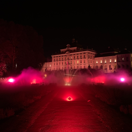 Zu sehen ist das rot angestrahlte Residenzschloss Ludwigsburg mit Wasserföntäne im Vordergrund