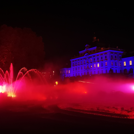 Zu sehen ist das blau und rot angestrahlte Residenzschloss Ludwigsburg mit einer Wasserfontäne