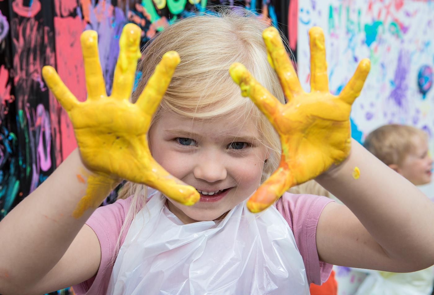 Mädchen zeigt ihre Handflächen, die voll gelber Fingerfarbe sind