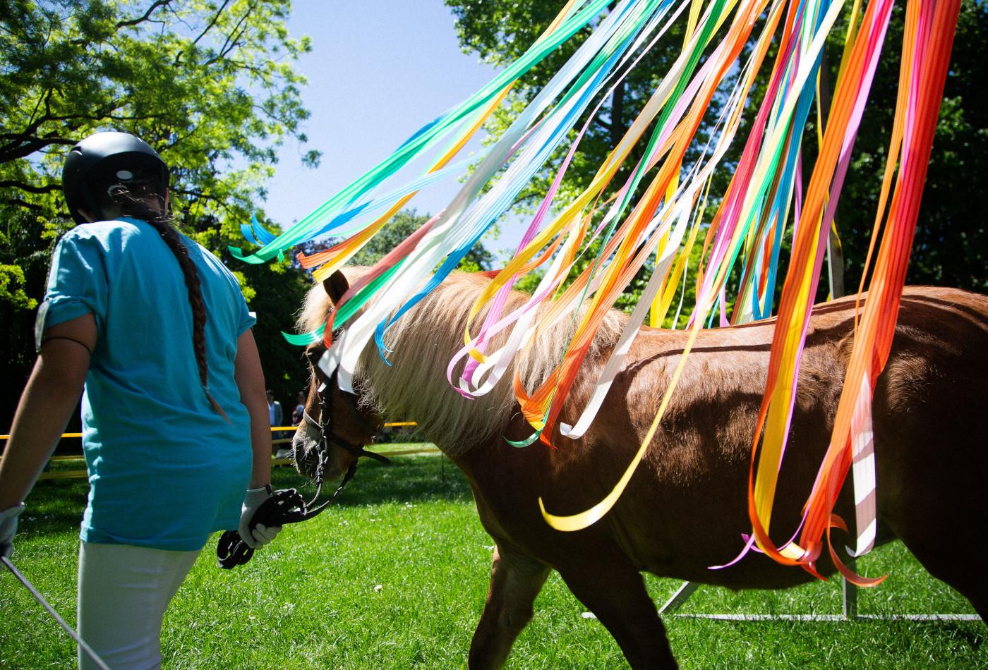 Kind führt ein Pony durch bunte, flatternde Bänder