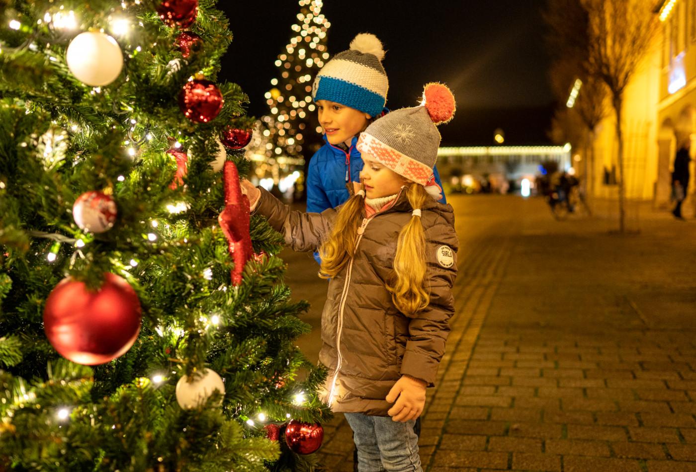 Mädchen und Junge bewundern einen prachtvoll geschmückten Weihnachtsbaum