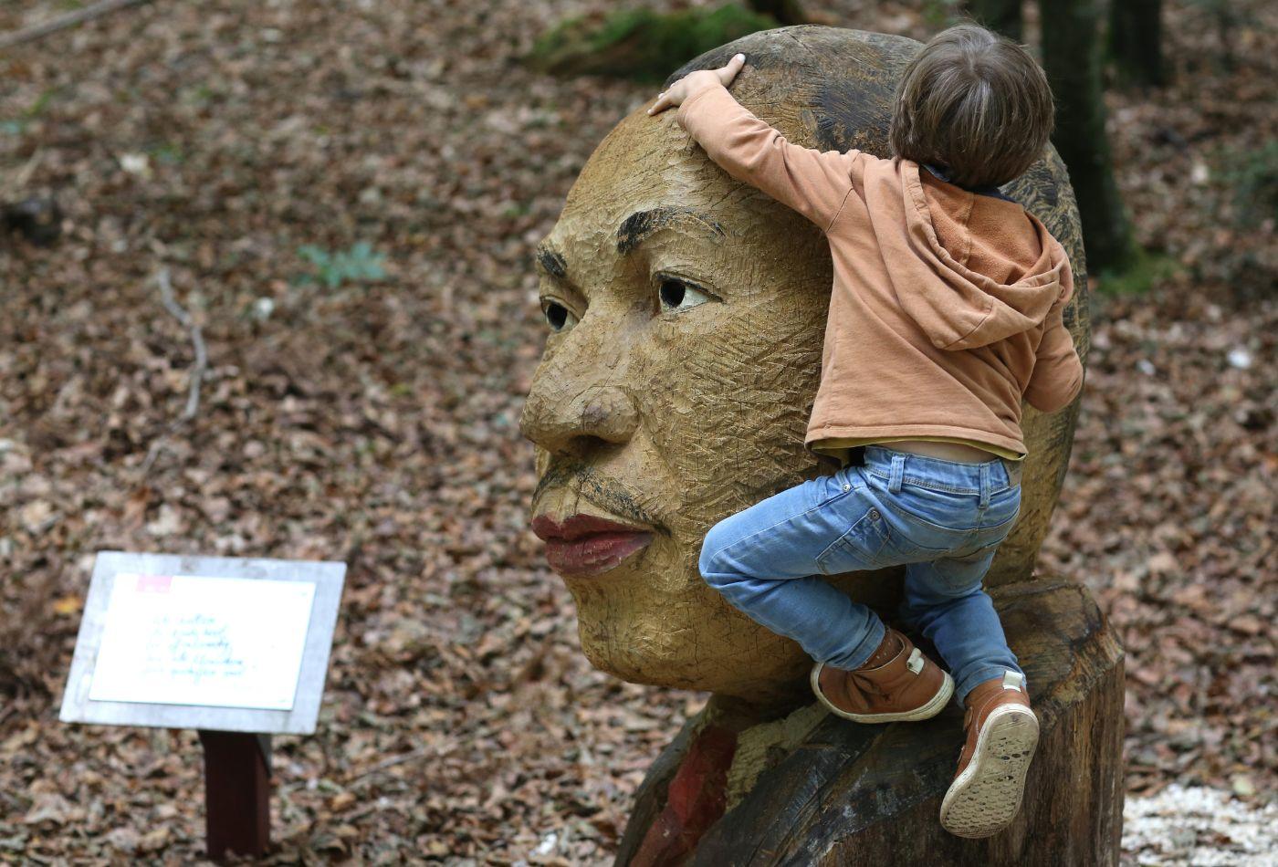 Ein Kind klettert auf eine große, hölzerne Skulptur, die einen Kopf darstellt