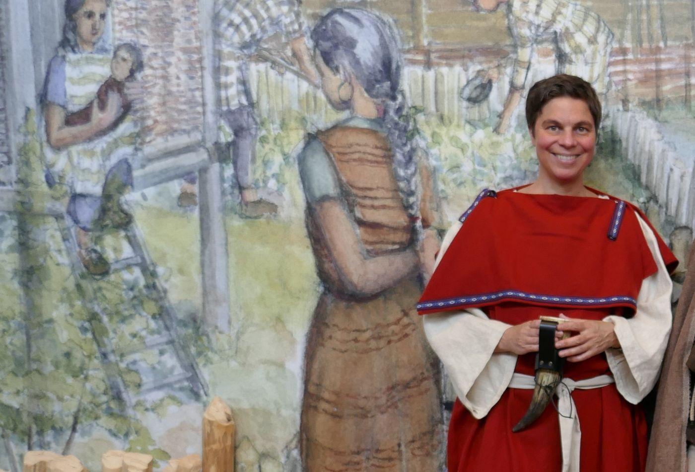 Eine Frau in keltischer Kleidung steht vor einem Wandgemälde im Keltenmuseum in Hochdorf an der Enz