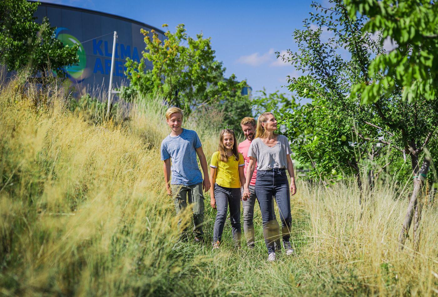 Eine Familie läuft durch eine Wiese mit Bäumen auf dem Außengelände der Klimaarena