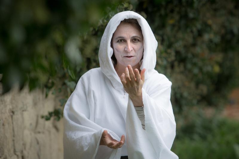 Eine Frau im weißen Gewand mit Kapuze und weißer Schminke im Gesicht blickt schaurig in die Kamera