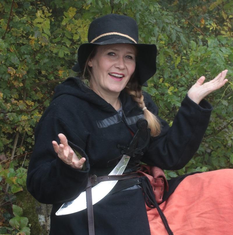 Auf dem Bild sieht man eine Räuberin mit schwarzem Hut und einem glänzenden silbernen Messer am Gürtel