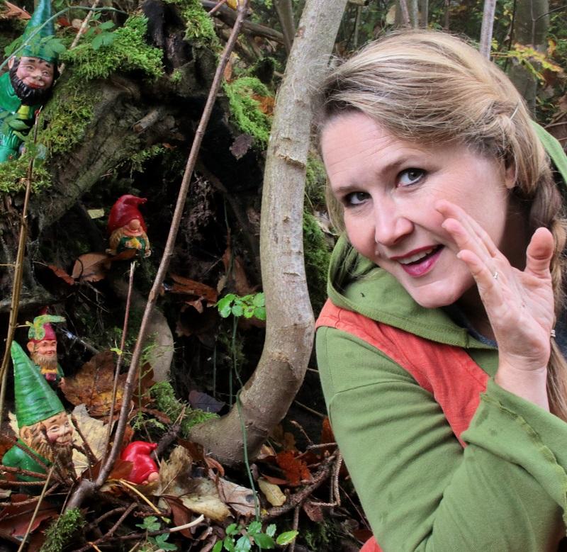 Märchenwanderung durch den Salonwald: Von Zwergenflüstern und Riesenschritten Auf dem Bild sieht man eine Märchenerzählerin, die geheimnisvoll flüstert, während im Hintergrund kleine Gartenzwerge auf dem Waldboden sitzen