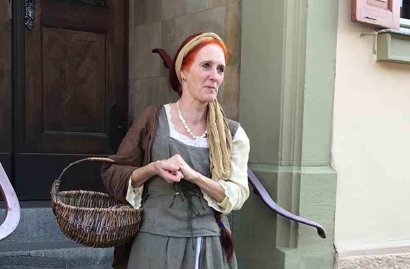 Eine historische Dame mit Haarband und Korb steht in einem Hauseingang
