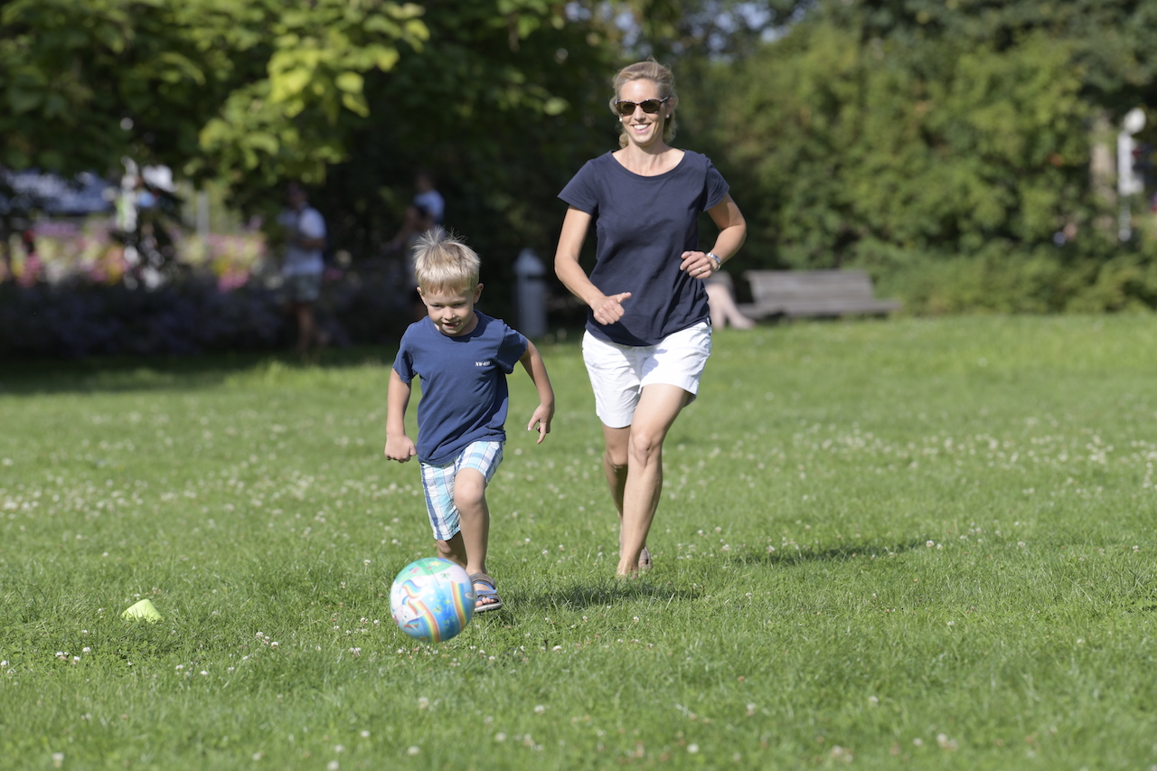 Mutter und Sohn rennen auf der Wiese beim Spielen einem Ball hinterher.