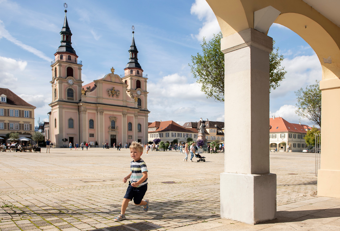 Kind läuft zwischen Arkaden am Marktplatz umher. Die evangelische Kirche im Hintergrund.