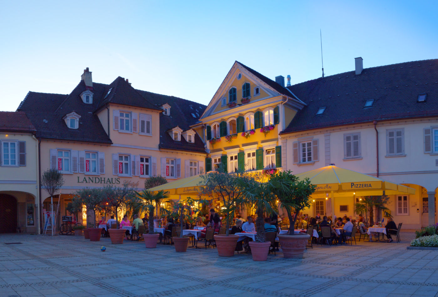 Blick auf ein Restaurant mit gelben Schirmen in Abendstimmung auf dem Marktplatz.
