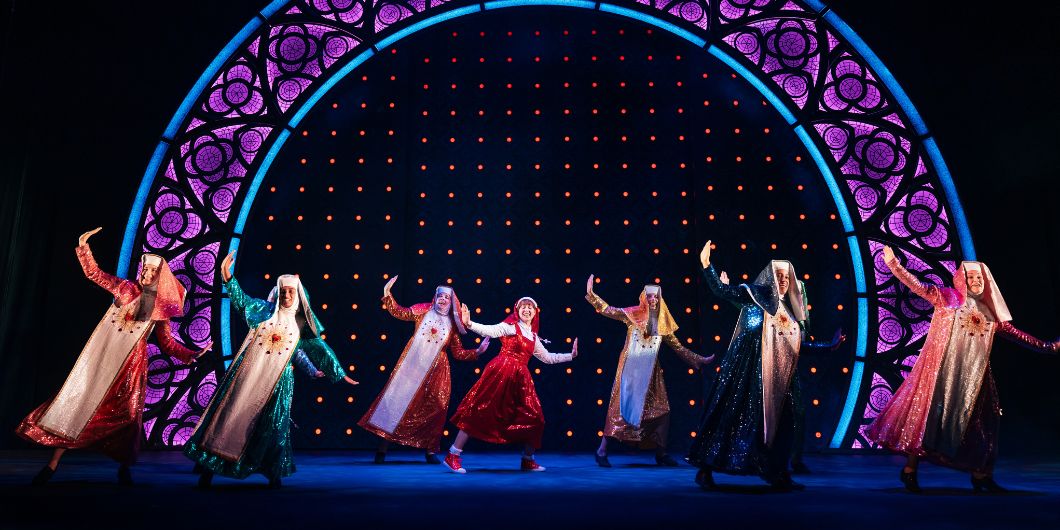 Sieben Nonnen tanzen auf der Bühne vor einer beleuchteten Kulisse