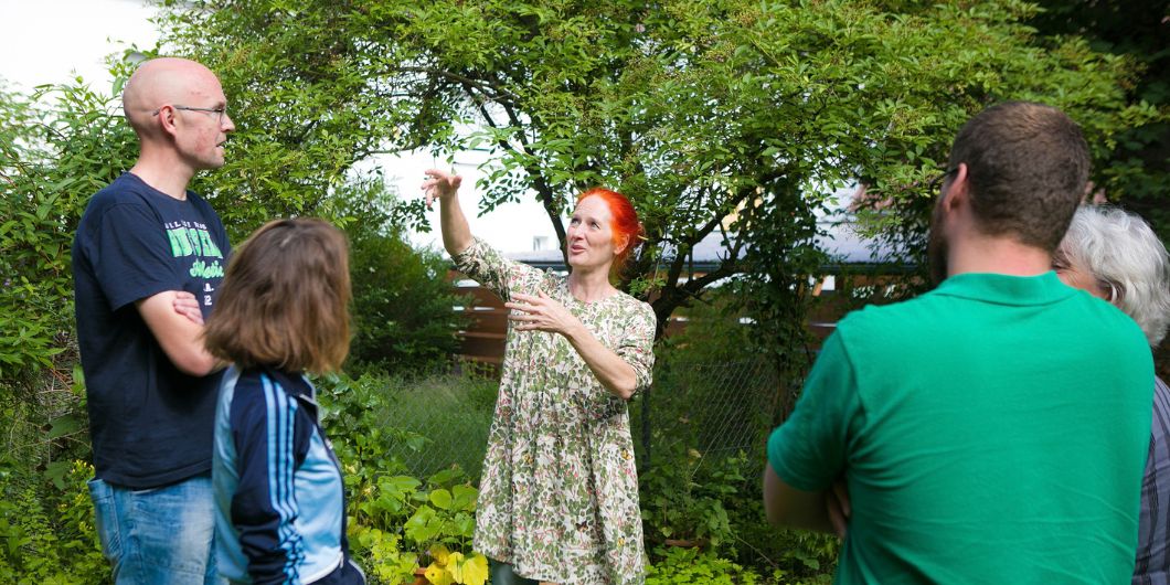 Vier Personen lauschen einer Stadtführerin. Sie stehen im Grünen.