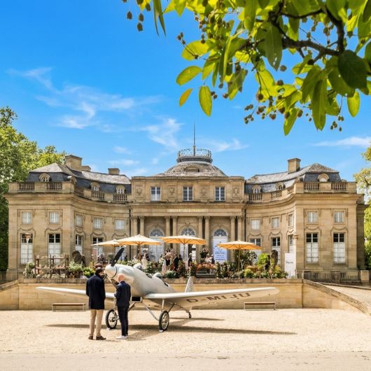 Vor dem Seeschloss Monrepos steht ein altes Motorflugzeug, das von zwei Personen betrachtet wird.
