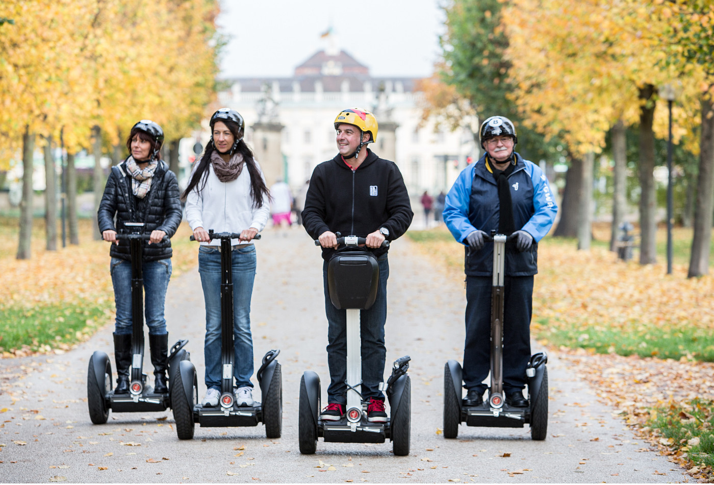 Vier Menschen fahren auf Segways auf der Königsallee, mit dem Residenzschloss Ludwigsburg im Hintergrund