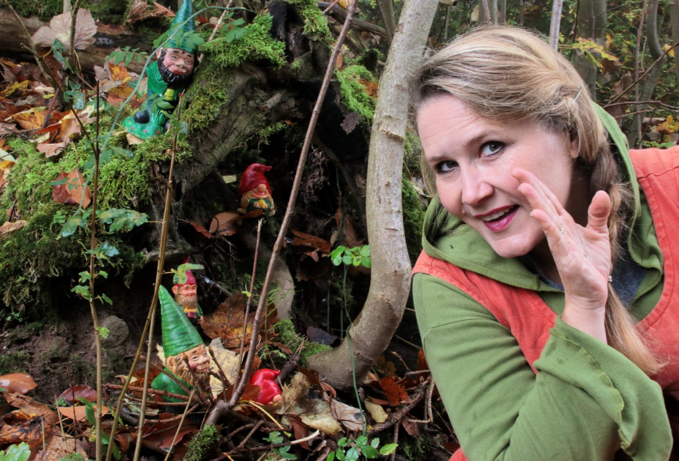 Märchenhexe Steffi hockt vor einer Baumwurzel, auf der Zwerge sitzen