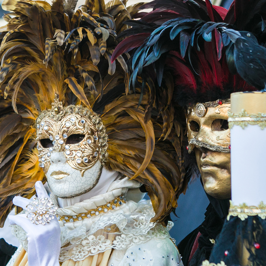 Zu sehen ist sind zwei kostümierte Personen im venezianischen Stil - eine schwarz-gold, die andere weiß-gold gekleidet.