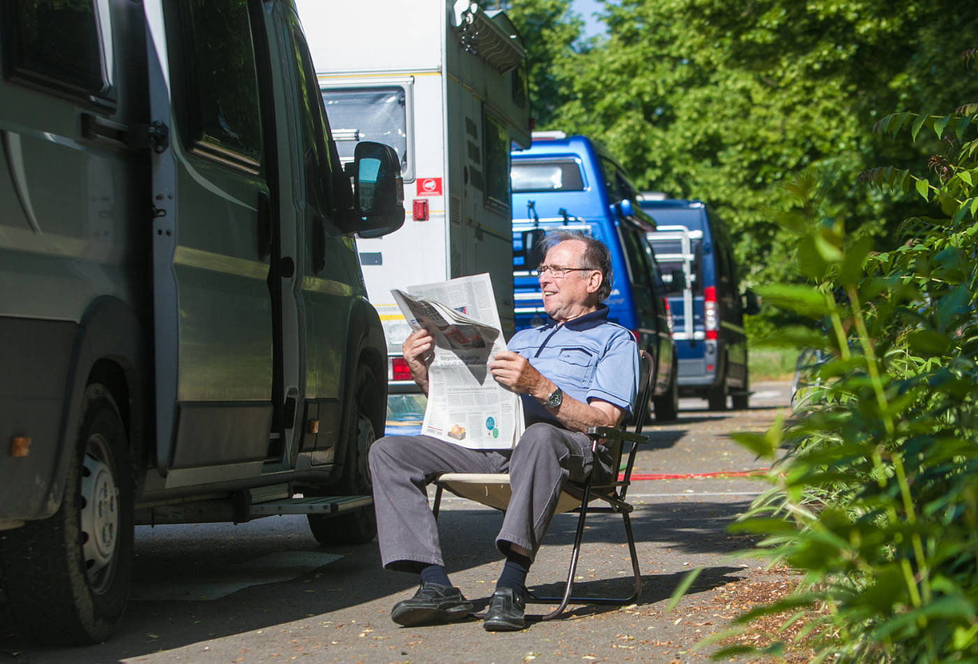 Ein Tourist sitzt Zeitung lesend vor seinem Wohnmobil