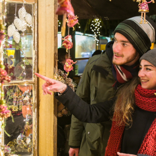 Zu sehen ist ein Pärchen, dass sich an einem Stand Weihnachtsschmuck ansieht.