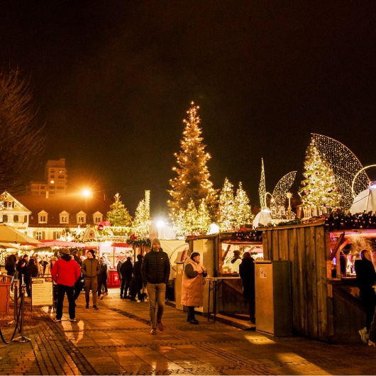 Zu sehen sind vier Personen, die an eine Tisch zusammenstehen und Glühwein trinken