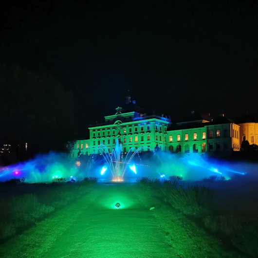 Zu sehen ist das grün und blau angestrahlte Residenzschloss Ludwigsburg inmitten schwarzer Nacht