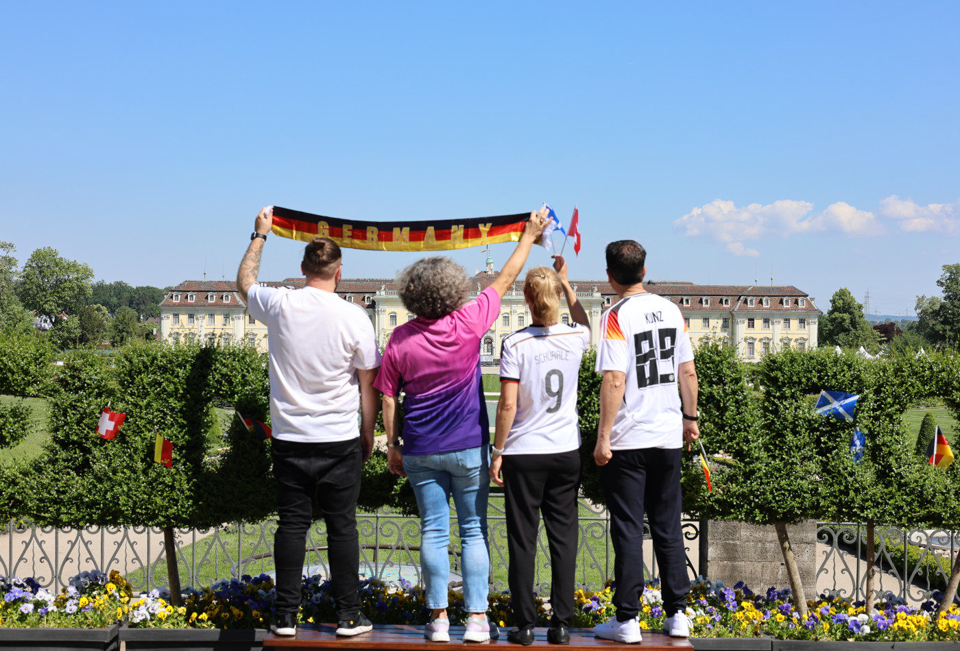 4 Personen in Fußballtrikots stehen mit dem Rücken zur Kamera, im Hintergrund das Residenzschloss Ludwigsburg 