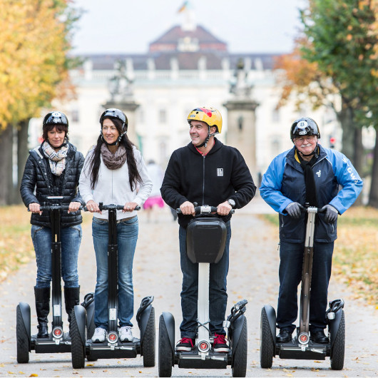 Vier Menschen fahren auf Segways über die Königsallee, im Hintergrund das Residenzschloss Ludwigsburg