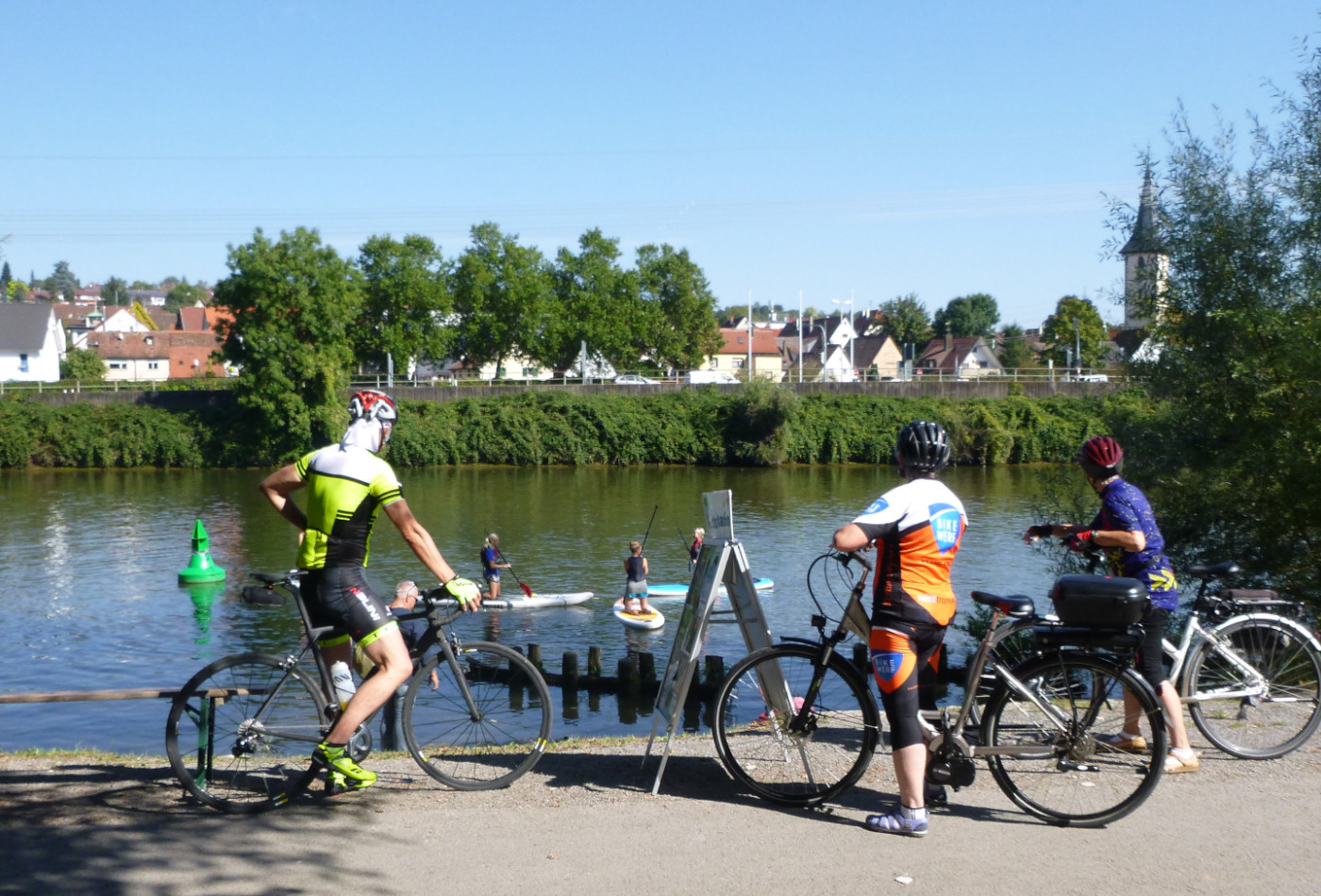 Drei Radfahrer, die Kanus auf dem Neckar betrachten.