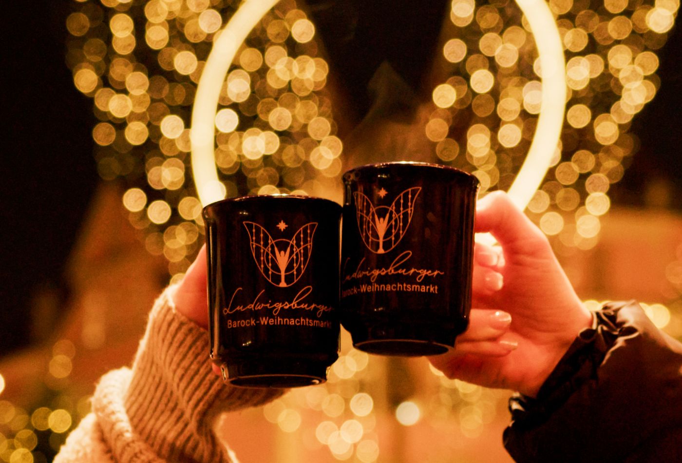 Weihnachtsmarkt_Glühweintassen Zwei Menschen stoßen mit Ihren Glühweintassen an
