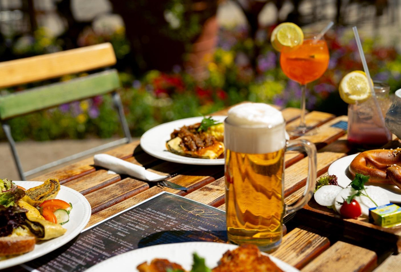 Blick auf einen gedeckten Biergarten-Tisch mit Bierglas, Cocktail und mehreren Gerichten