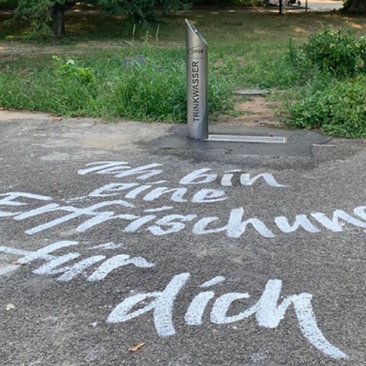 Trinkbrunnen mit dem Schriftzug "Ich bin eine Erfrischung für dich" auf dem Boden 