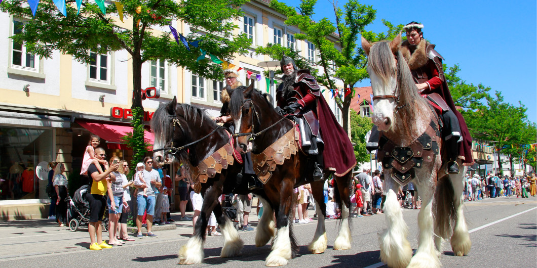 Drei Reiter in Rüstung reiten auf großen Pferden beim Pferdeumzug