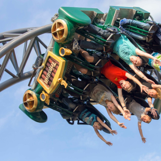 Fahrender Achterbahnwagon mit Menschen darin, der gerade über Kopf steht.