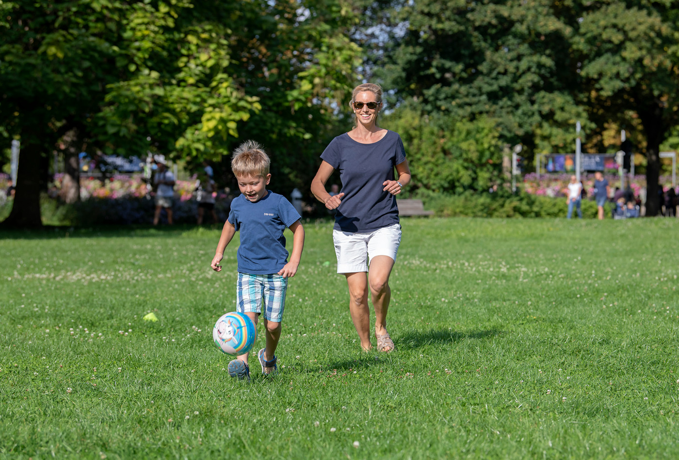 Mutter und Kind spielen mit einem Ball auf einer grünen Wiese.