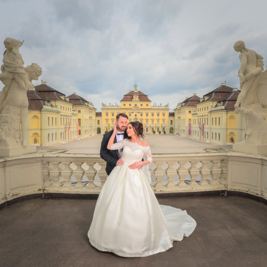 Ein Brautpaar posiert für das Foto auf dem Balkon des Residenzschlosses, im Hintergrund der Ehrenhhofof