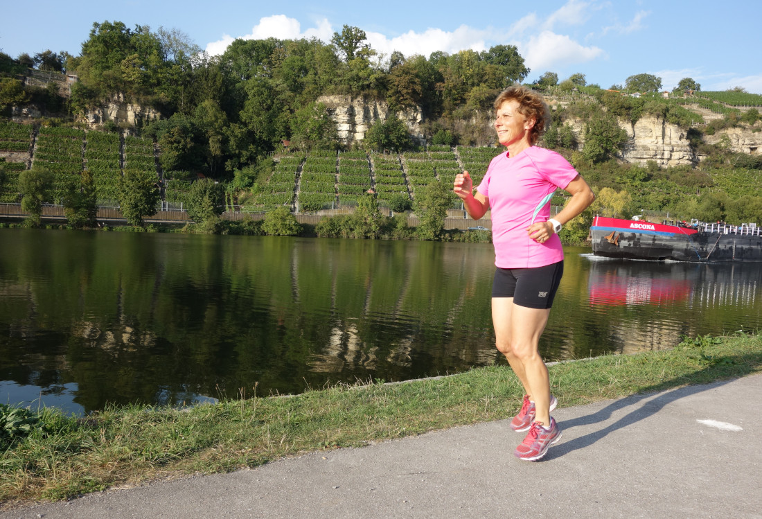Eine Frau joggt entlang des Neckarufers.