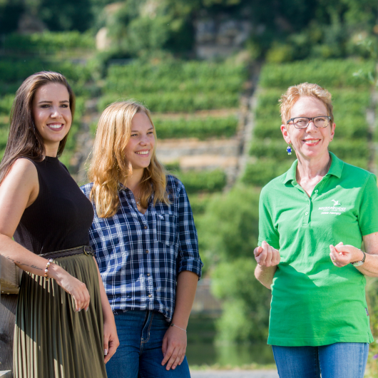 Zu sehen sind drei Personen vor den Weinbergen.