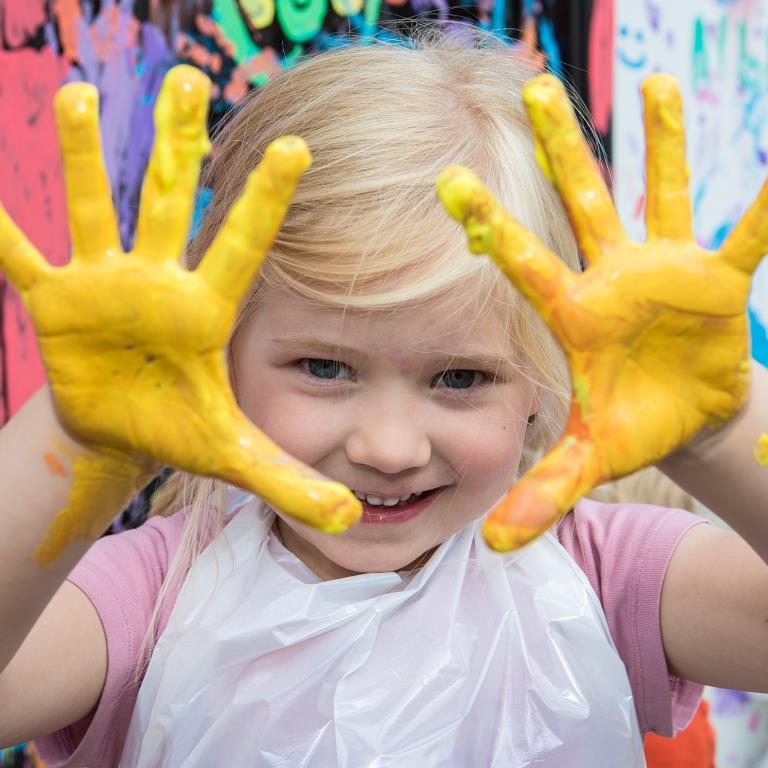 Kind streckt gelb bemalte Hände in die Kamera