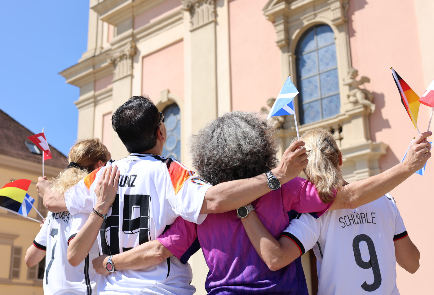4 Personen in Fußballtrikots stehen mit dem Rücken zur Kamera vor der Stadtkirche Ludwigsburg