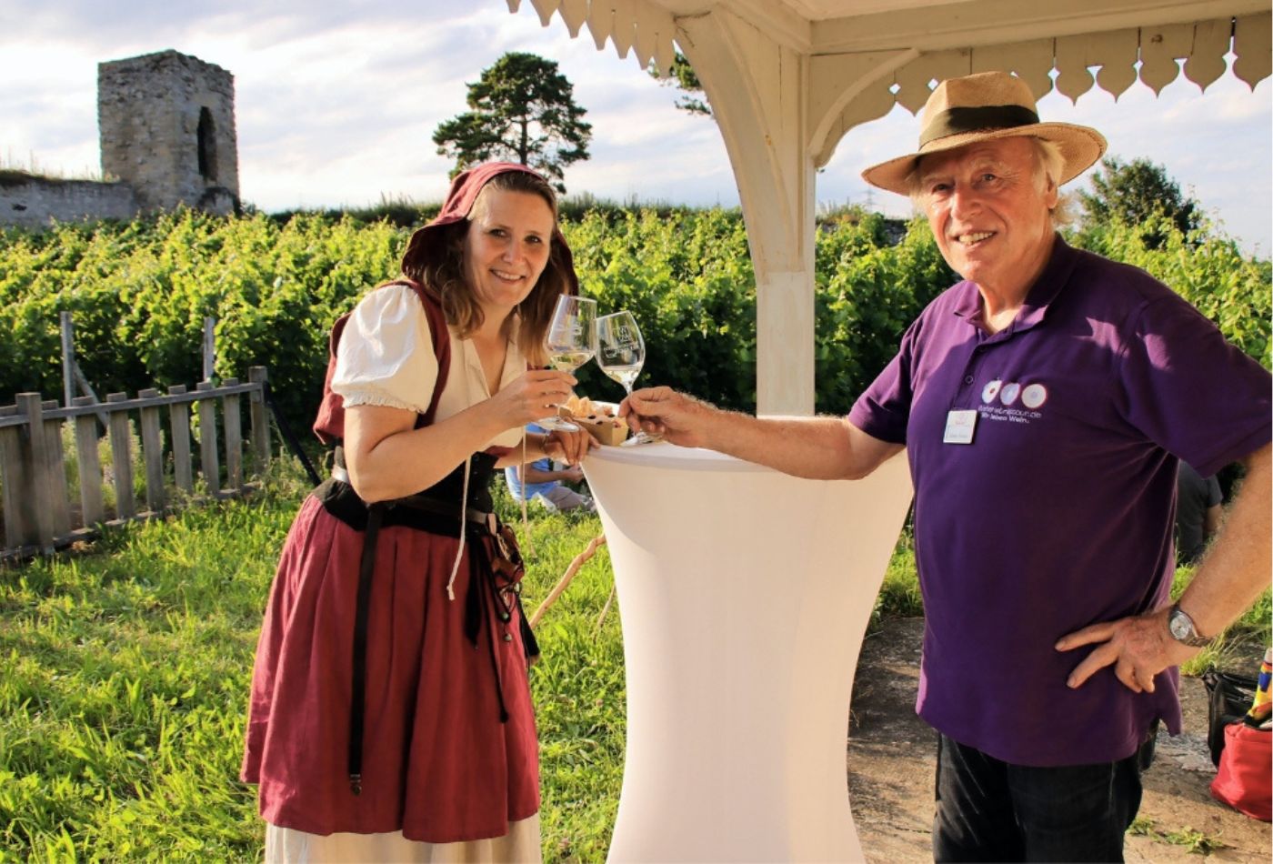 Durch zwei blühende Büsche schaut man auf die Tische und Stühle des Biergartens