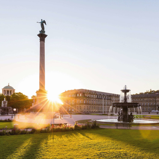Statue und Brunnen vor dem Neuen Schloss Stuttgart im Sonnenuntergang.