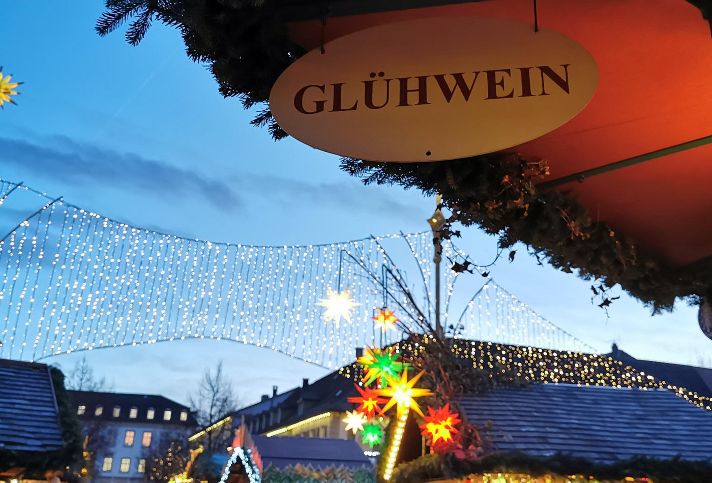 Glühwein Schild vor Lichtern der Weihnachstmarkt Buden