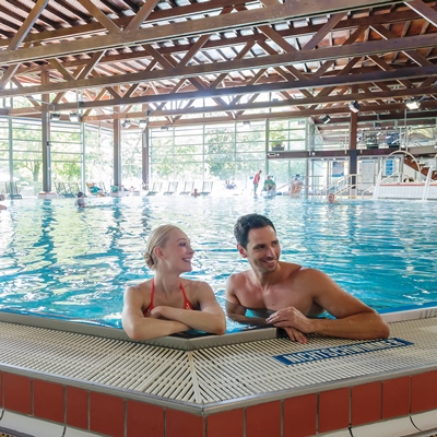 Zwei Menschen sind in einem Becken im Heilbad Hoheneck mit blauem Wasser. Sie lachen.