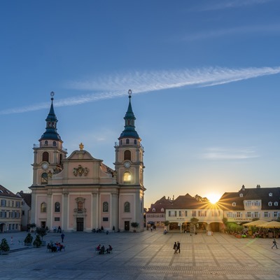 Blick auf den Marktplatz im Vordergrund Menschen, im Hintergrund die evangelische Stadtkirche und die letzten Sonnenstrahlen am Abend