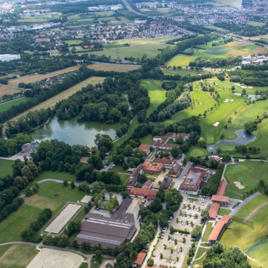 Luftaufnahme einer grünen Landschaft mit einem See und einigen Häusern.