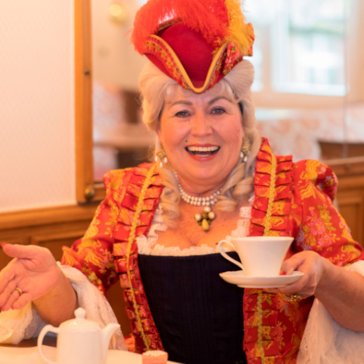 Eine Frau im Kostüm sitzt in eine Café und hält eine Tasse.