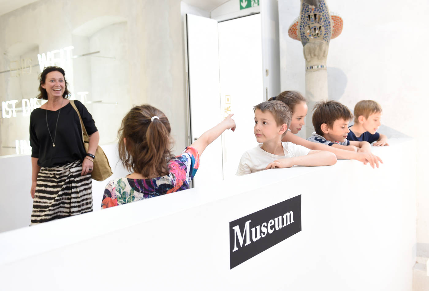 Kinder stehen an einer weißen Brüstung in einem Museum.