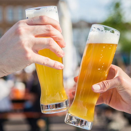 Man sieht zwei Hände, die mit gefüllten Biergläsern anstoßen
