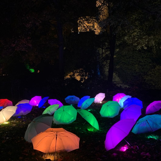 Zu sehen sind leuchtende, bunte Regenschirme im dunkeln