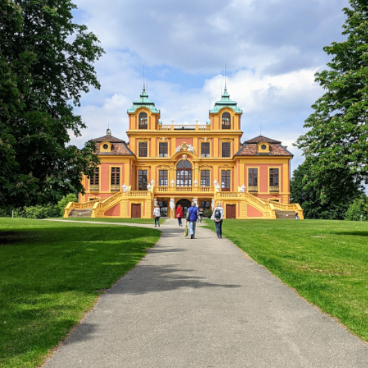 Zu sehen ist eine Gruppe Spaziergänger vor dem Schloss Favorite.